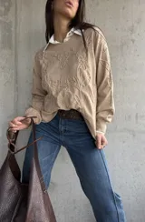 Sweater de punto color beige con diseño bordado en relieve de flores y hojas. Presenta cuello redondo, mangas largas con puños acanalados y un corte holgado.