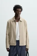 Cazadora color beige de algodón, corte recto, con cuello solapa, cierre frontal con cremallera, manga larga con puños abotonados y bolsillos laterales de ojal.