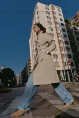 Trench largo de color negro con cuello de solapa, cierre frontal cruzado con botones y cinturón ajustable a tono. Presenta mangas largas con trabillas en los puños, bolsillos delanteros de vivo y abertura en la espalda.