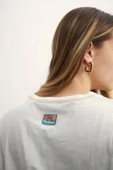 Remera color crema de corte holgado, con mangas cortas y costuras a la vista en color ocre.