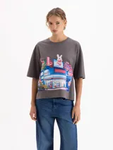 Remera de algodón color gris con estampa gráfica frontal de estilo anime que representa un mercado con un conejo. Presenta un corte amplio, cuello redondo y mangas cortas.