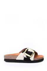 Sandalia tipo zueco con capellada de cuero con pelo estampado animal print de vaca en blanco y negro. Presenta una hebilla metálica dorada grande en el empeine, plantilla anatómica de corcho y suela de goma negra.