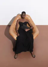 Vestido largo de fiesta color negro, con escote palabra de honor y diseño evasé. Presenta múltiples niveles con volantes decorativos y cierre lateral con cremallera.