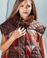 Chaleco sin mangas de diseño híbrido que combina paneles de tela acolchada capitoné en color azul marino con secciones de tejido de lana a cuadros en tonos naranja, gris y negro. Presenta cuello con forro de piel sintética marrón, cierre frontal con cremallera y ribetes en color rojo vibrante. Incluye bolsillos delanteros amplios con cierre.