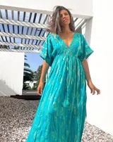 Túnica larga de color turquesa con estampado de arabescos en tono dorado. Presenta un escote en V profundo, mangas cortas amplias y un cordón ajustable en la cintura con terminaciones de borlas.