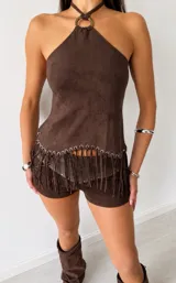 Top marrón de gamuza sintética con escote halter y detalle de argolla metálica en el cuello. Presenta flecos en el ruedo con ojalillos metálicos.