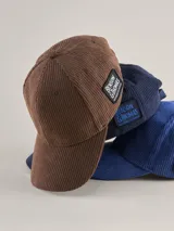 Gorra tipo baseball confeccionada en pana color azul marino, con parche rectangular lateral que incluye el logo de la marca Benson & Thomas.