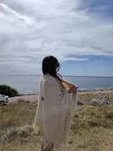 Ruana triangular tejida a crochet color crema con flecos largos.