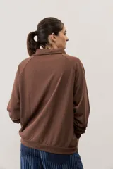 Buzo celeste de manga larga con cuello polo y cierre frontal de botones. Presenta un parche marrón bordado en el pecho.