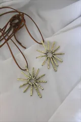 Collar con colgante dorado en forma de sol y tira de cuero sintético marrón.