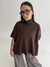 Poncho de tejido de punto color marrón chocolate, con cuello alto tipo polera y mangas cortas amplias. Presenta un diseño holgado con terminaciones acanaladas en el ruedo.