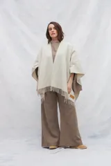 Ruana de lana sin teñir, color beige claro con finas rayas verticales en tono marrón. Presenta flecos en el borde inferior y un forro interior en tono marrón.