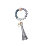 Llavero con pulsera de cuentas redondas en tonos de gris y madera, con borla decorativa gris y gancho metálico dorado.