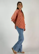 Blusa color beige con cuello mao, mangas 3/4 con puños elásticos y detalle de diseño geométrico texturizado en el frente.