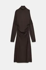 Vestido midi de punto color marrón, con cuello subido, manga larga y diseño cut out en un hombro. Presenta frunces laterales en la cintura que aportan un efecto drapeado.