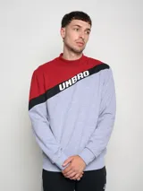 Buzo de hombre con diseño de bloques de color, combinando rojo en la parte superior de los hombros y gris melange en el cuerpo. Presenta una franja diagonal negra con el logo Umbro en blanco cruzando el pecho.