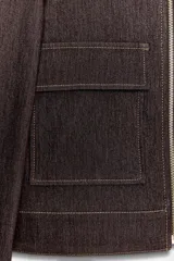 Chaqueta corta de denim oscuro con cuello solapa, cierre frontal con cremallera y bolsillos delanteros de plastrón con solapa. Presenta mangas largas con hombreras y costuras a la vista.