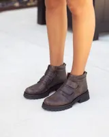 Botines de cuero marrón oscuro con efecto desgastado y suela track negra gruesa. El calzado se ajusta mediante dos tiras de velcro en el empeine.