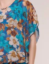 Blusa de gasa semitransparente con hilos de lúrex, diseño estampado floral en tonos blanco, gris y negro, silueta holgada tipo capa y escote redondo con detalle metálico.