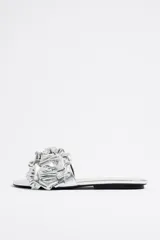 Sandalias plateadas con base plana y adorno de flores con volados en el empeine.