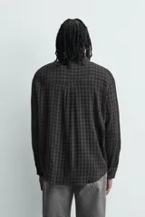 Camisa de corte relajado con diseño de cuadros en tonos negro y beige, cuello camisero, manga larga y cierre frontal de botones.