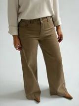 Jean de corte recto y tiro medio, en color camel con acabado desgastado. Presenta diseño clásico de cinco bolsillos, cierre frontal con botón y cremallera, y costuras reforzadas en el ruedo.