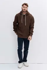 Buzo con capucha tipo canguro confeccionado en tela de corduroy color marrón. Presenta cordones blancos en contraste, bolsillo frontal tipo canguro y logo bordado sutil en el pecho.