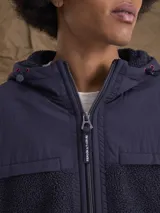 Campera con capucha confeccionada en una combinación de tejido técnico y sherpa, con cierre frontal completo y puños elásticos.
