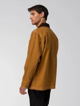 Chaqueta tipo chore de Caterpillar, color marrón con cuello en contraste, cierre frontal de botones y cuatro bolsillos de parche frontales. Presenta pespuntes en contraste y etiqueta de marca en el pecho.