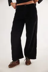 Pantalón de pana color negro con corte de pierna ancha y tiro medio-bajo. Presenta bolsillos delanteros y traseros, un pin bordado de la marca y un aplique cuadrado decorativo en una de las piernas.