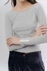 Remera básica de manga larga en color gris melange, con escote bote y detalle de aplique en el puño.