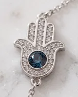 Pulsera de cadena fina con dije central en forma de mano de Hamsa, decorado con pavé de cristales y un cristal central azul oscuro.