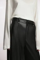 Pantalón de tiro alto efecto piel en color marrón, con pierna ancha y costuras marcadas en la parte delantera. Presenta trabillas en la cintura y cierre frontal con cremallera, botón y gancho metálico.