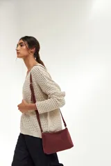 Bandolera pequeña de cuero gamuzado color bordó, con correa larga regulable y cierre superior.
