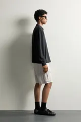 Bermuda cargo color negro de corte relaxed fit, confeccionada en tejido de algodón con elasticidad y efecto lavado. Cuenta con cintura elástica ajustable con cordón, bolsillos frontales y bolsillos laterales tipo cargo con solapa en las perneras.
