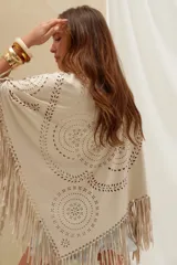 Poncho de gamuza color crudo, con diseño calado en patrones geométricos y florales, y terminación de flecos largos en todo el borde.