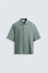 Camisa de lino color negro con calce relajado, cuello bowling y manga corta. Presenta cierre frontal con botones a tono y aberturas laterales en el bajo.