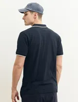 Remera polo azul marino con ribetes blancos en el cuello y en los bordes de las mangas corta, y cierre frontal de botones.