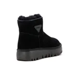 Pantubota de cuero negro con interior forrado en lana natural, suela de goma dentada y aplique triangular con logo en el lateral.