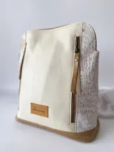 Mochila de cuero color beige y blanco, con detalles laterales texturizados, bolsillos frontales verticales con cierre y asas ajustables.