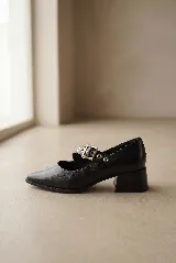 Zapato tipo Mary Jane de gamuza color marrón, con taco cuadrado medio y tira ajustable con hebilla metálica y ojalillos decorativos.