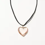 Collar con colgante de vidrio transparente en forma de corazón, engarzado con alambre dorado y cadena de gamuza sintética negra.