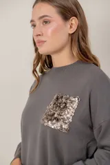 Sweater negro de punto con cuello redondo, mangas largas y un bolsillo frontal decorado con lentejuelas brillantes.