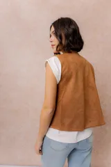 Chaleco corto de efecto gamuza color tostado, con detalles bordados en contraste en los bordes y en la parte inferior. Presenta escote en V y diseño abierto al frente.