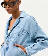 Campera de jean oversized de corte amplio con recortes estructurales, cierre frontal con botones metálicos, cuello clásico y bolsillos frontales.