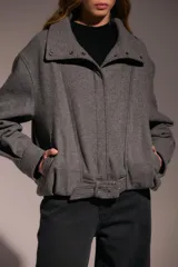 Campera bomber de paño gris con cuello alto, cierre frontal con botones a presión y cinturón integrado en el ruedo.