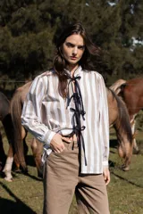Camisa de algodón con estampado de rayas verticales en tonos beige y blanco. Presenta un diseño de cuello mao con cierre frontal mediante cintas negras, mangas largas con frunces en los hombros y puños abotonados.