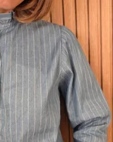 Camisa de algodón color blanco, con cuello alto con volados, mangas tres cuartos con detalles de bordado ingles y cierre frontal con botones de nácar.