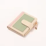 Billetera compacta de mujer, con diseño color block en rosa, verde menta y beige. Tiene cierre de cremallera y un broche frontal. Incluye un charm dorado en forma de imperdible con un dije de flor.