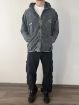 Campera con capucha y cierre frontal, de color gris con efecto lavado ácido. Presenta bolsillos frontales tipo canguro y logotipos bordados en el pecho.